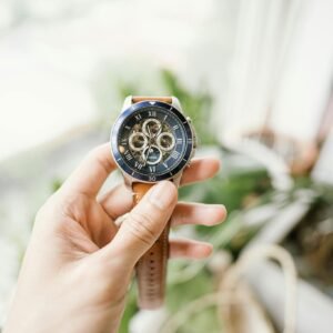 A hand holding a sophisticated wristwatch with intricate gears, featuring a blurred background.