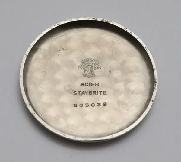 Vintage watch back cover with engravings and logo on a grey background.