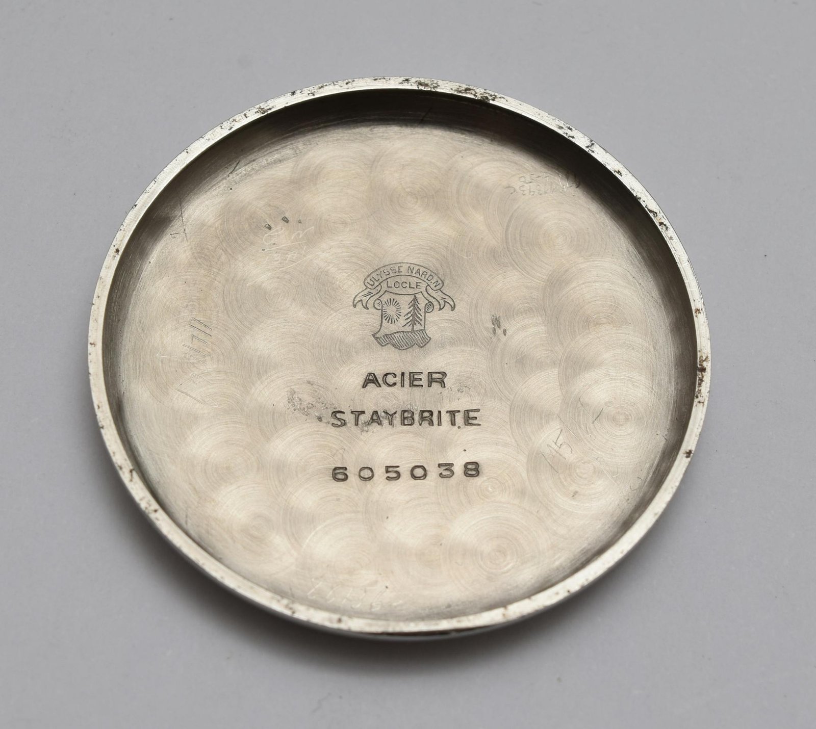 Vintage watch back cover with engravings and logo on a grey background.